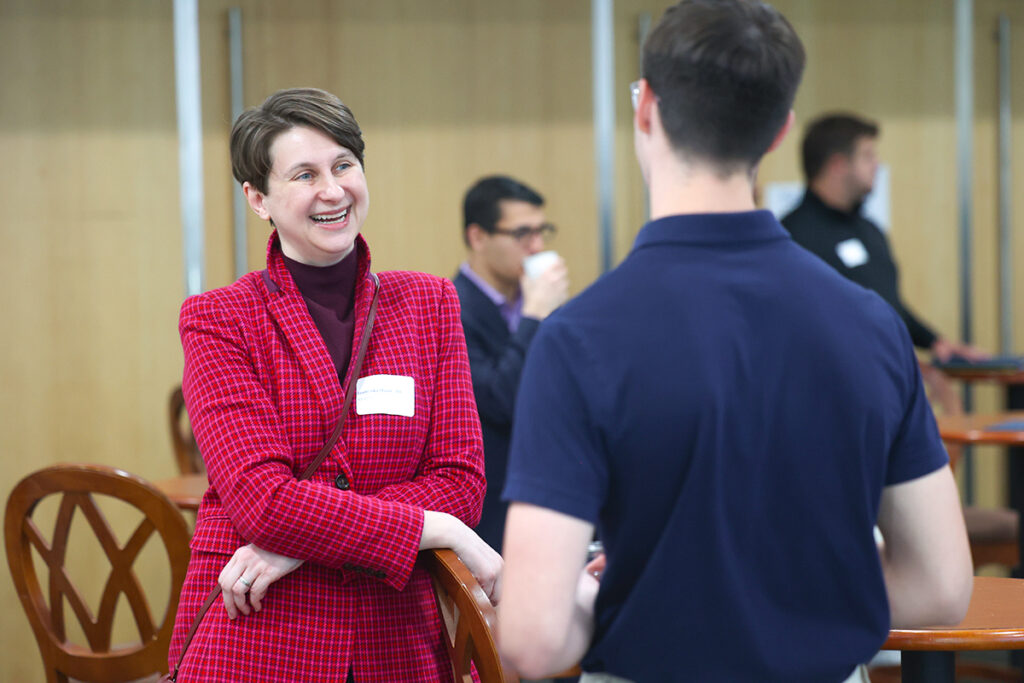 Professional in a red jacket speaking with a student during a networking session.