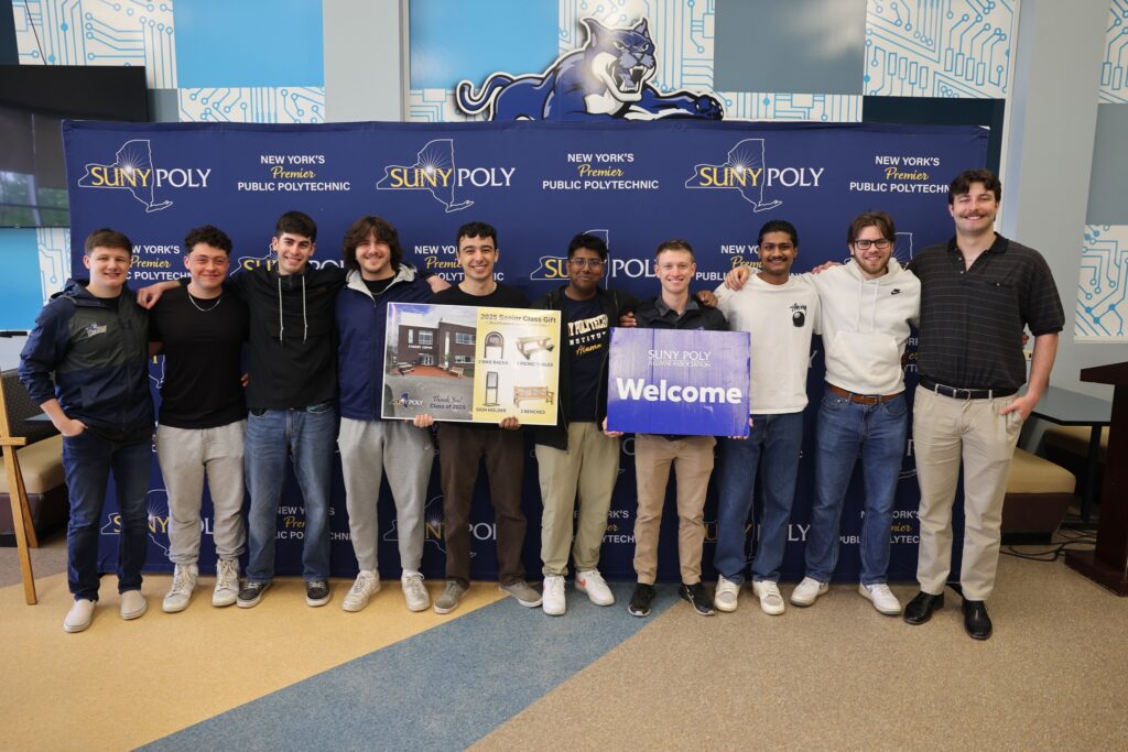 Group of graduates holding their class gift and SUNY Poly Welcome sign.