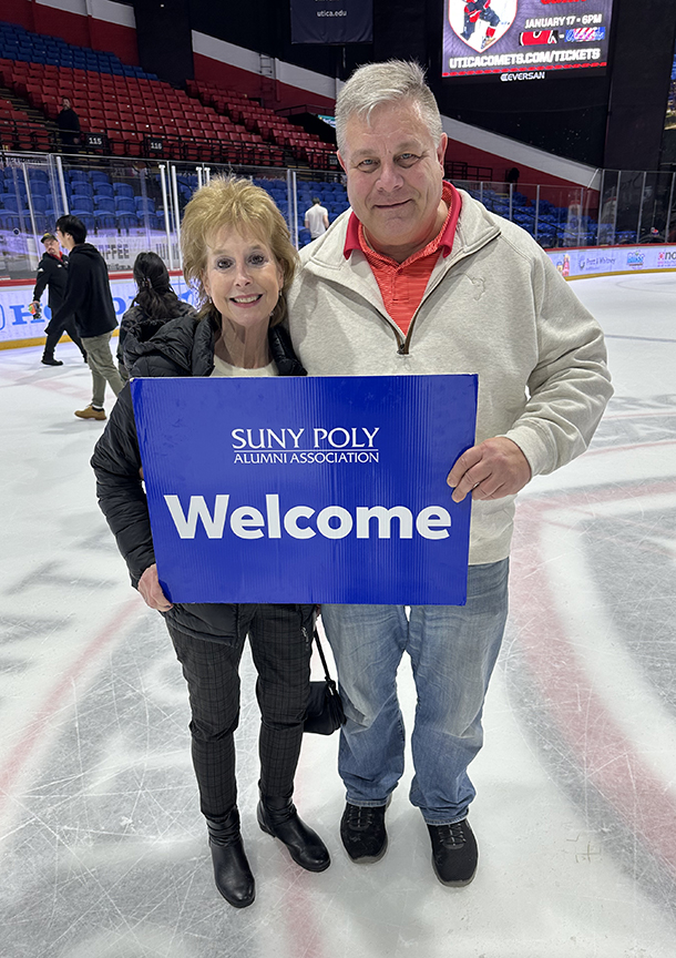 Two people holding the SUNY Poly Alumni Association Welcome sign on center ice.