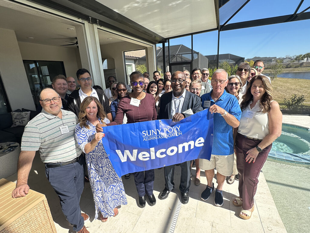 Alumni and staff gathered and holding a Welcome banner.